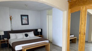 Quarto de hotel com cama, mesas de cabeceira, um espelho e um banco de madeira.
