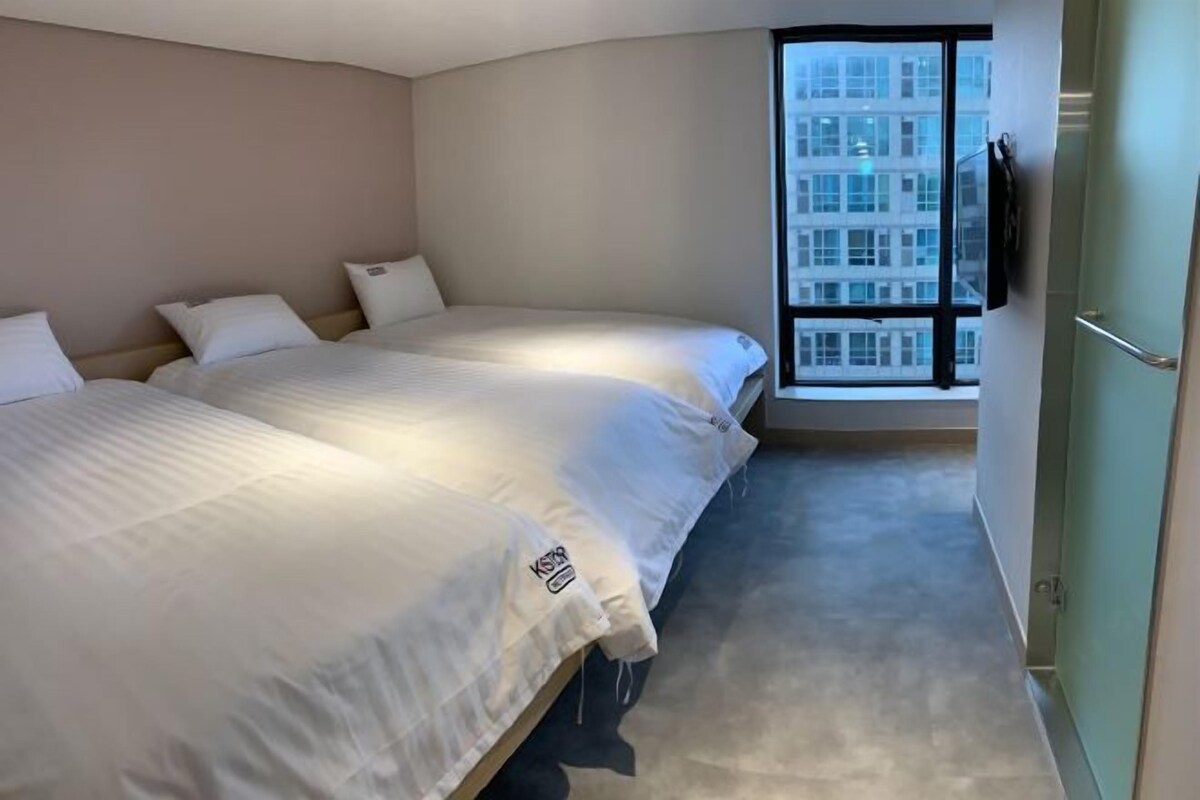 A hotel room with two beds, a large window, and a view of a building.