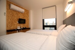 Une chambre d’hôtel avec deux lits, un téléviseur fixé au mur, un climatiseur et une fenêtre donnant sur la ville.