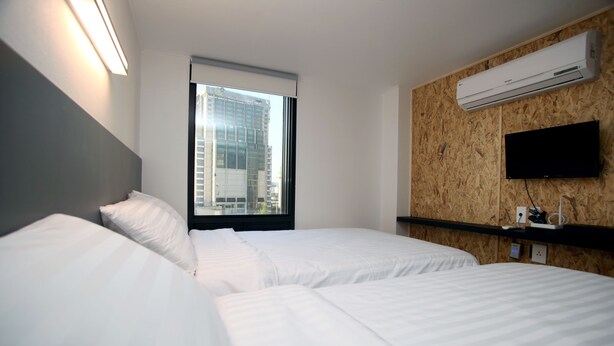 A hotel room with two beds, a large window with a city view, an air conditioning unit, and a mounted television. - KSTAR Metro Hotel (Seoul)
