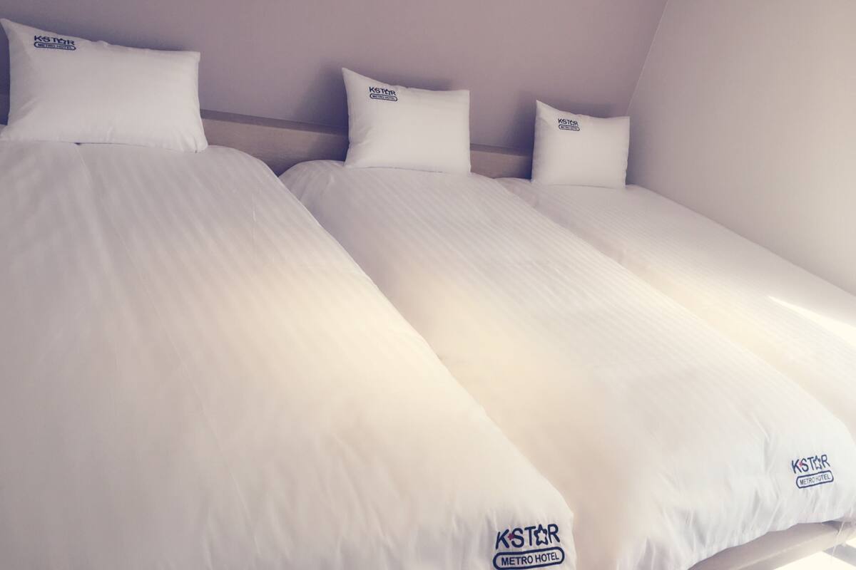 Two single beds with white bedding and pillows, each with a KSTOR METRO HOTEL logo.