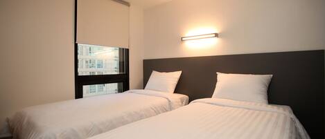 Une chambre d’hôtel avec deux lits simples, une fenêtre avec des stores et un luminaire fixé au mur.