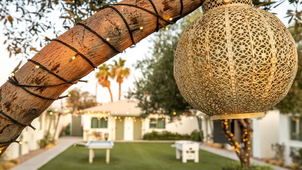 Une lanterne décorative suspendue, ornée de motifs complexes, une branche en bois illuminée et une pelouse bien entretenue agrémentée de mobilier d’extérieur.