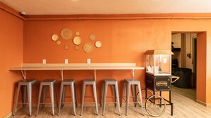 Une pièce avec un mur orange, une longue table avec des tabourets de bar et un chariot à pop-corn.
