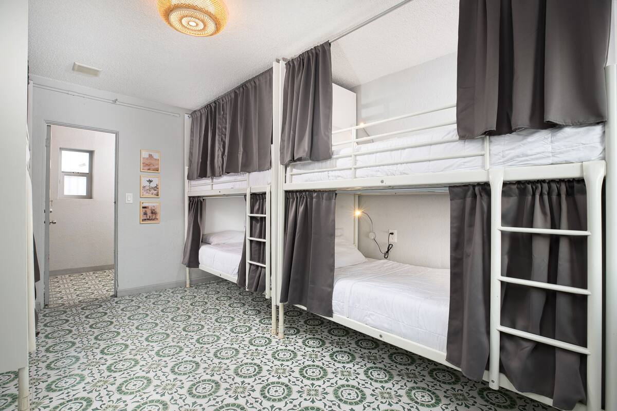 A dormitory room with bunk beds, patterned floor tiles, and a door leading to another room.