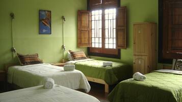 A room with two beds, each with a green bedspread and white linens, a wooden cabinet, and a window with wooden shutters.
