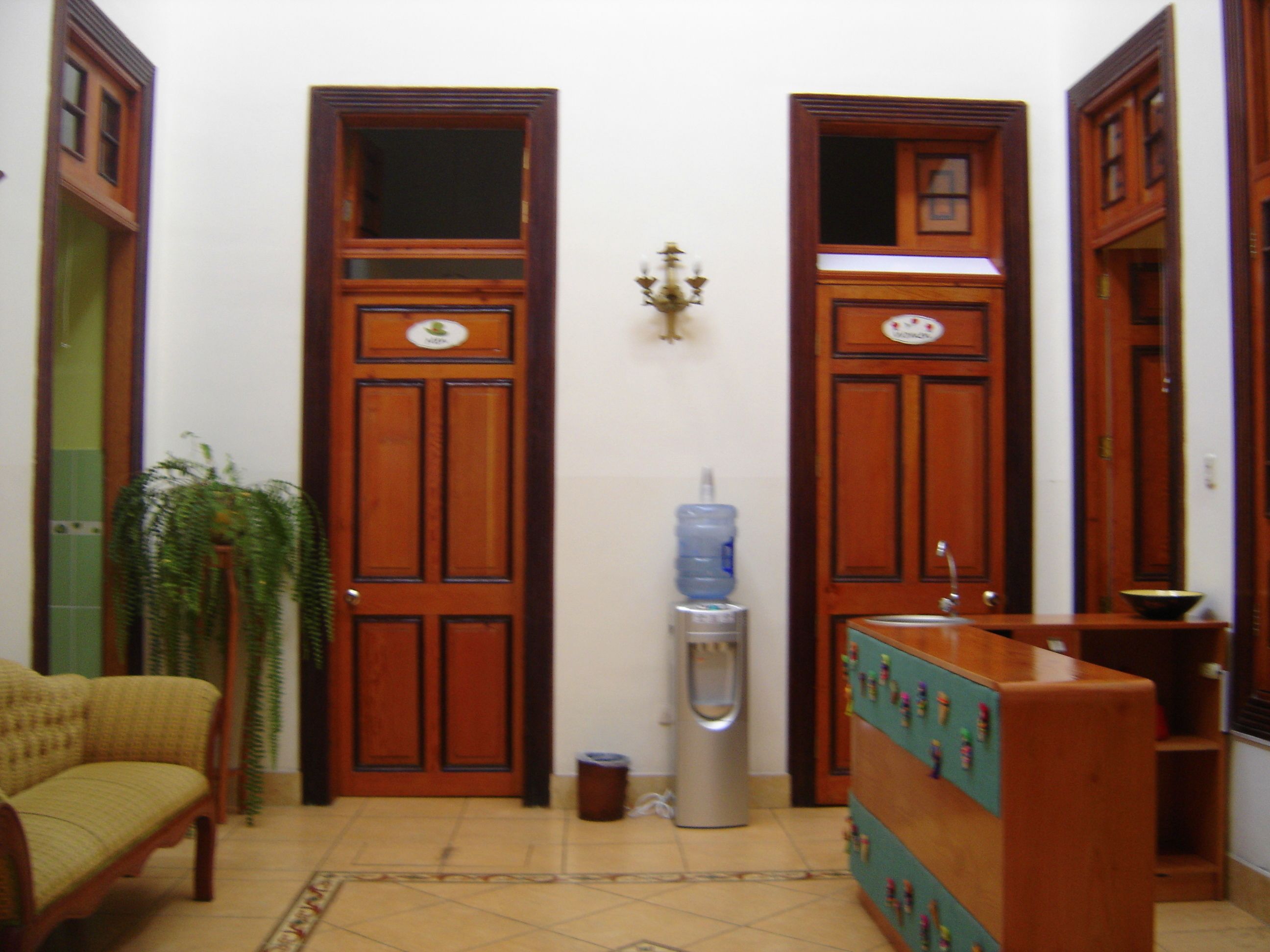 A hallway with wooden doors, a water dispenser, a trash bin, a sofa, and a decorative plant.