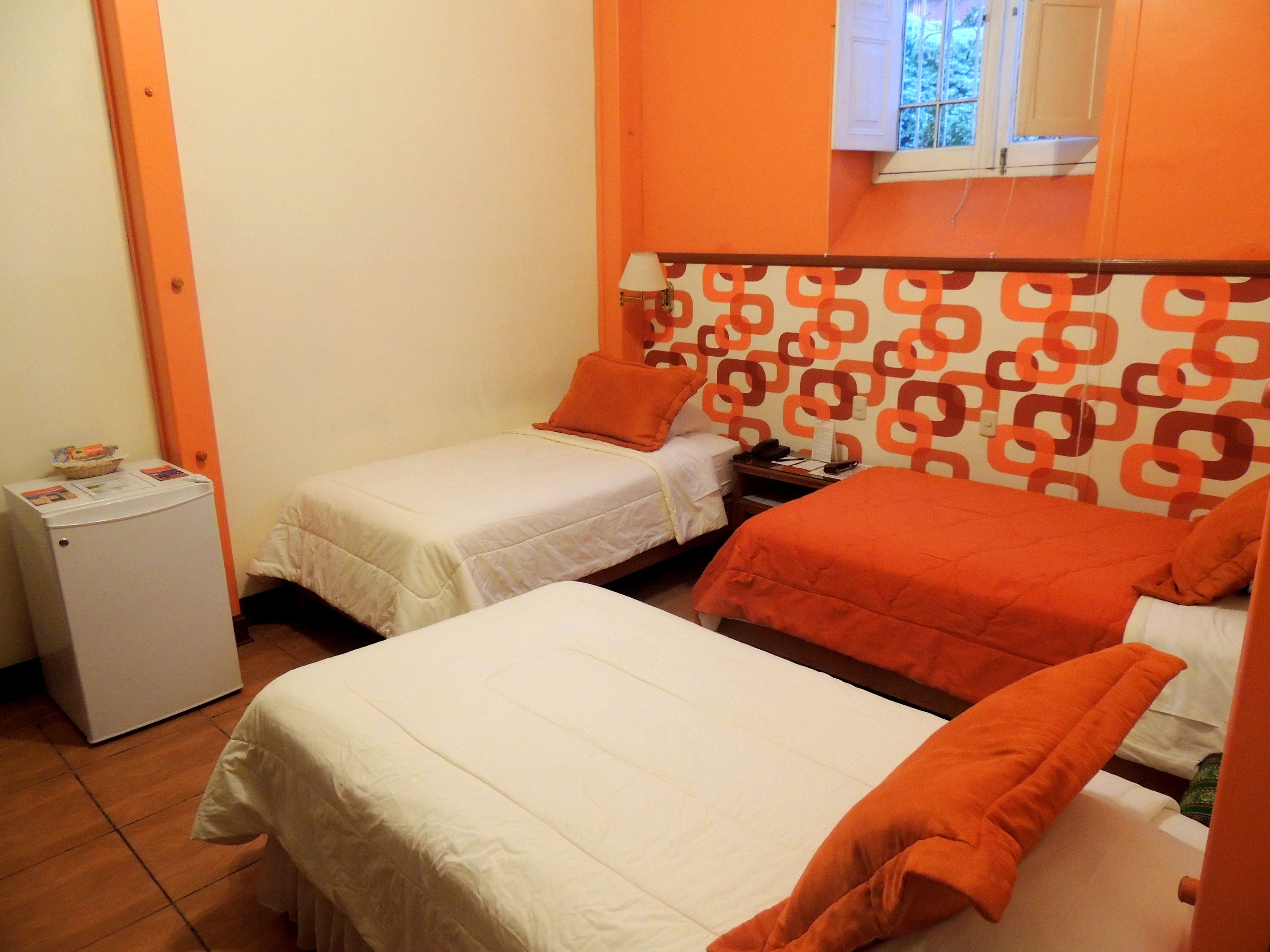 A small hotel room with two single beds, a small refrigerator, and a window with a view.