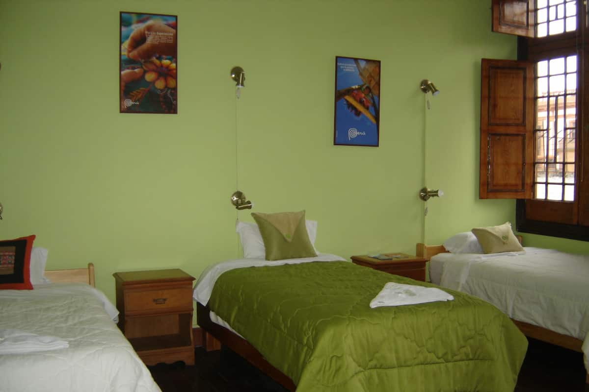 A hotel room with two single beds, a wooden nightstand, a green bedspread, and two wall-mounted lamps.