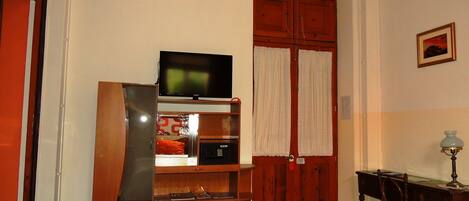 Un espacio habitable compacto con un mueble de madera, un televisor, un microondas y una zona de comedor con mesa y sillas.