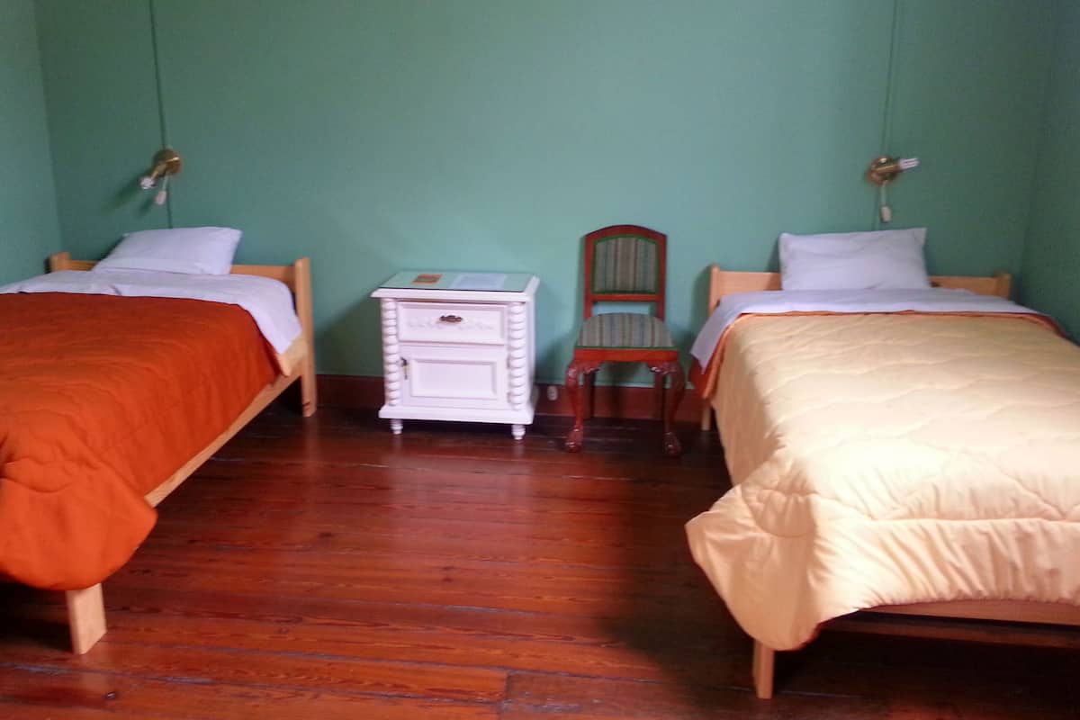 A room with two single beds, a small white dresser, a chair, and a nightstand with lamps.
