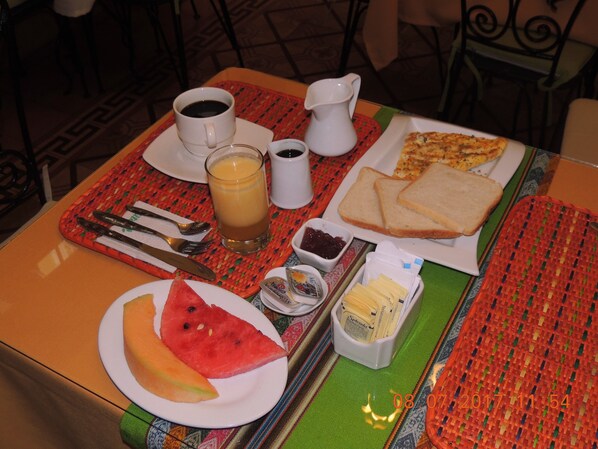 A table with breakfast items including toast, a slice of watermelon, a glass of orange juice, a cup of coffee, and a small container of jam. - Lima Wari Hotel Boutique (Lima)