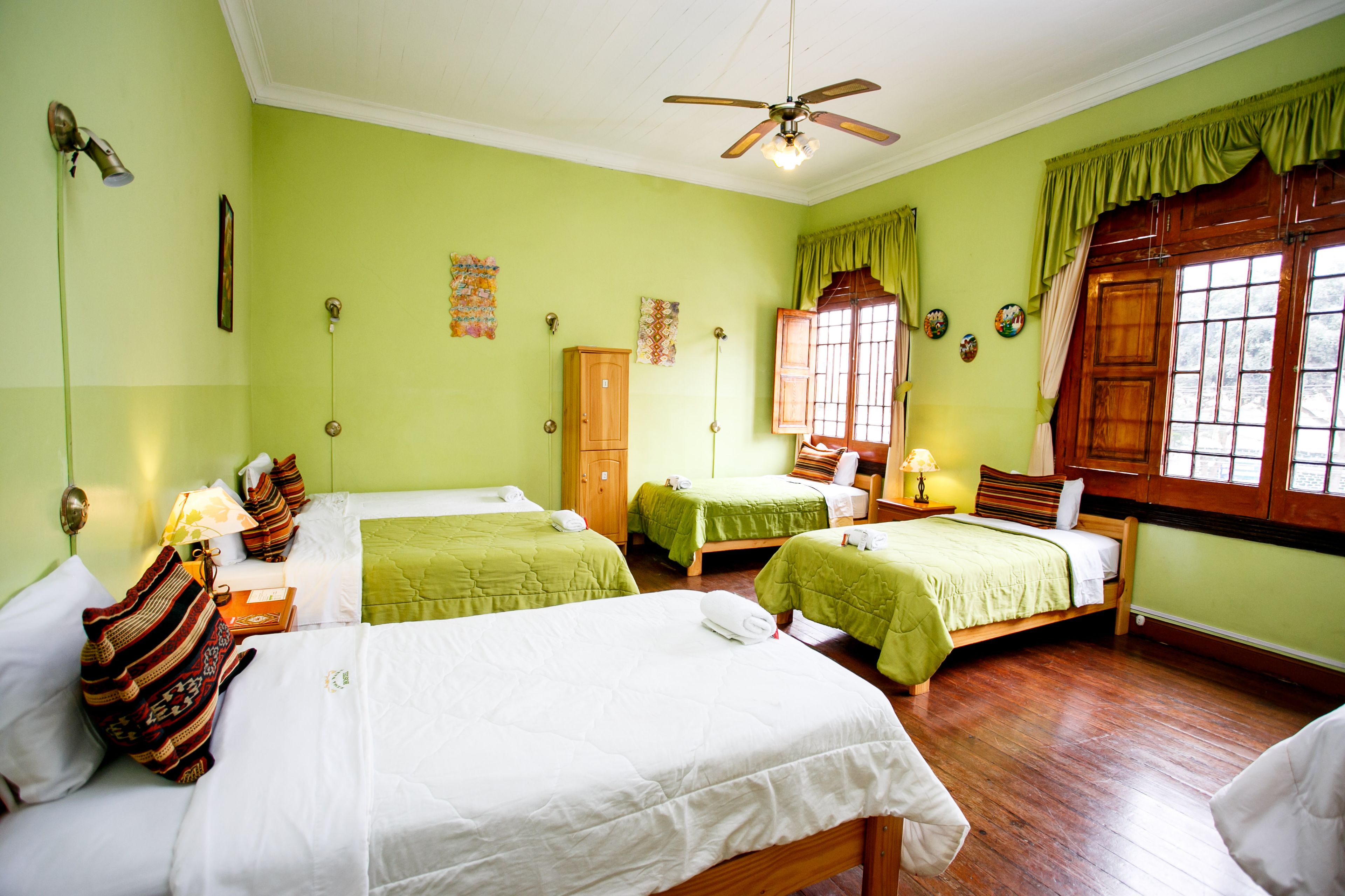 A hotel room with three beds, a wooden wardrobe, a ceiling fan, and a window with curtains.