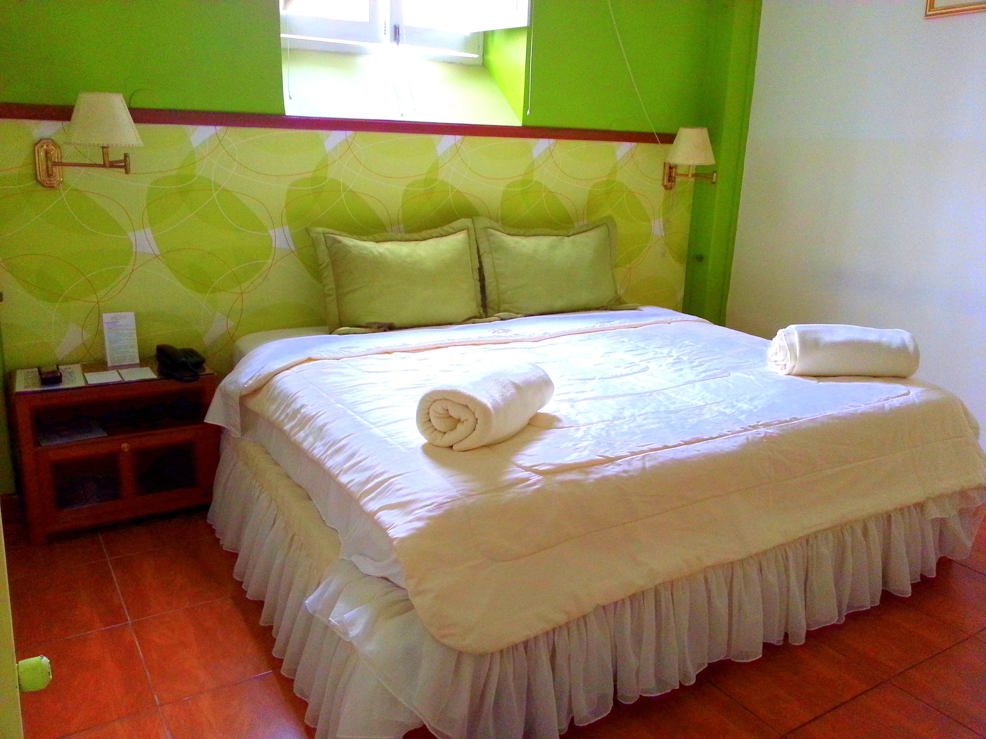 A neatly made bed with a rolled towel, a nightstand with a lamp, and a wall with a geometric pattern.