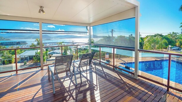 A covered outdoor area with a pool, chairs, and a view of a body of water and distant landscape.