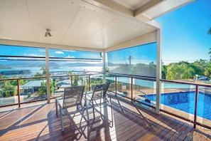 A covered outdoor area with a pool, chairs, and a view of a body of water and distant landscape.