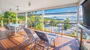 A balcony with a table and chairs, a view of a body of water, and greenery.