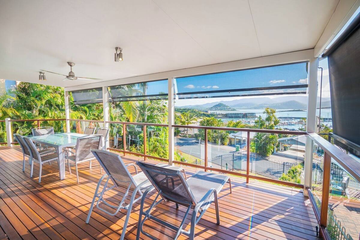 Een balkon met een tafel en stoelen, uitzicht op water en begroeiing.