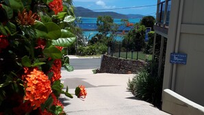 A pathway leading to a building with a view of the sea and mountains. There is a sign indicating the building is for apartments.