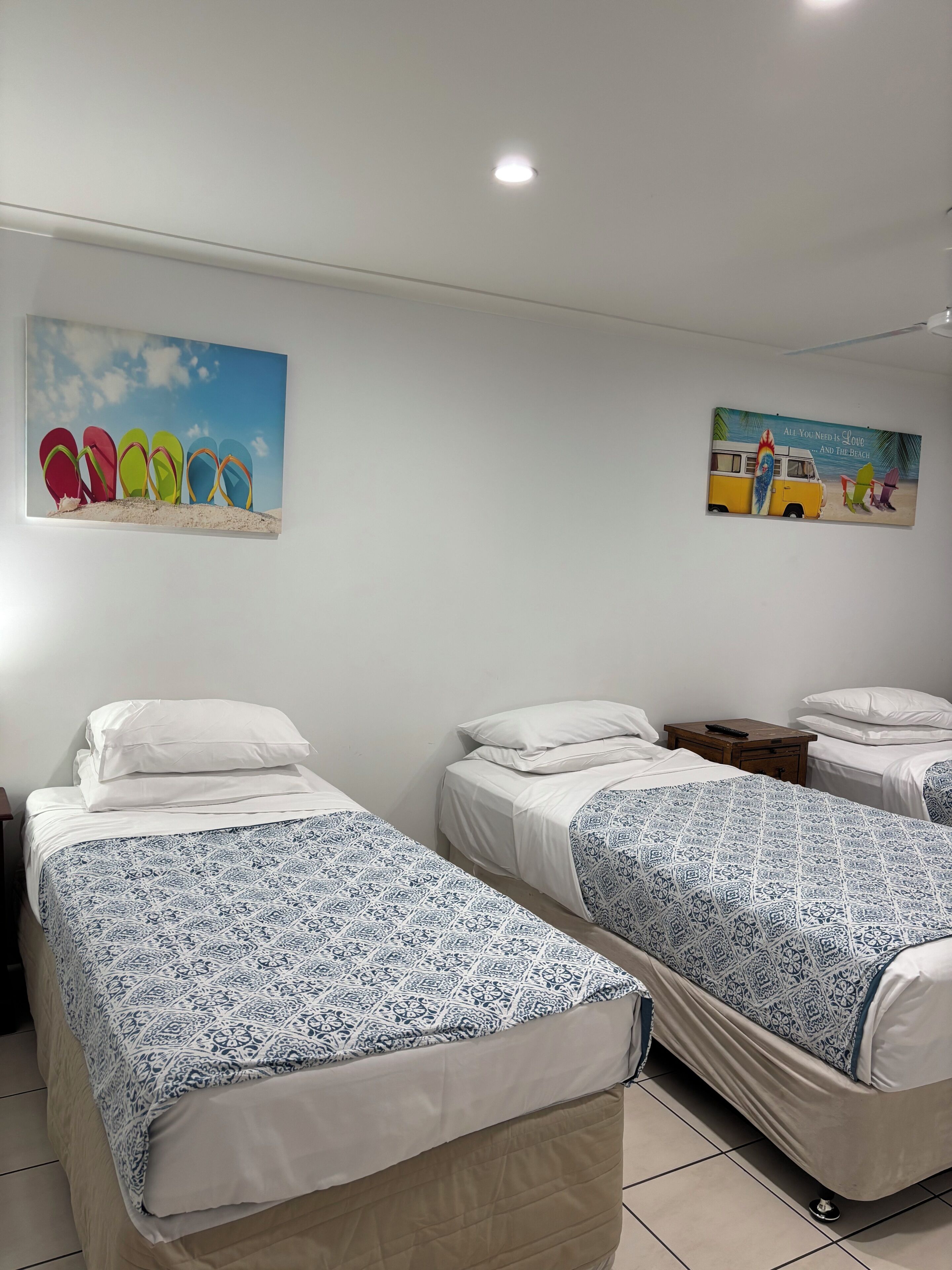 A hotel room with two beds, a painting of flip-flops and a van, and a ceiling light.