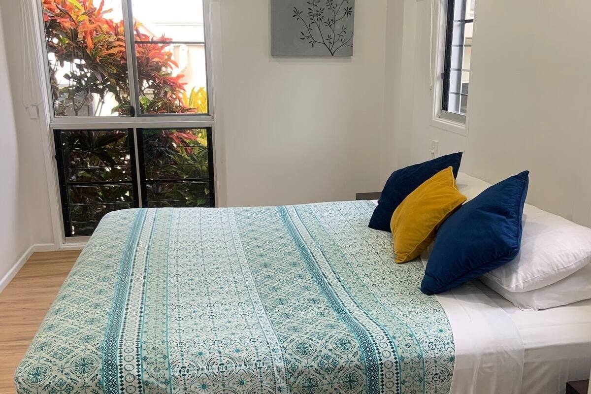 Een slaapkamer met een bed, een raam met uitzicht op begroeiing, een airconditioning en een plafondventilator.