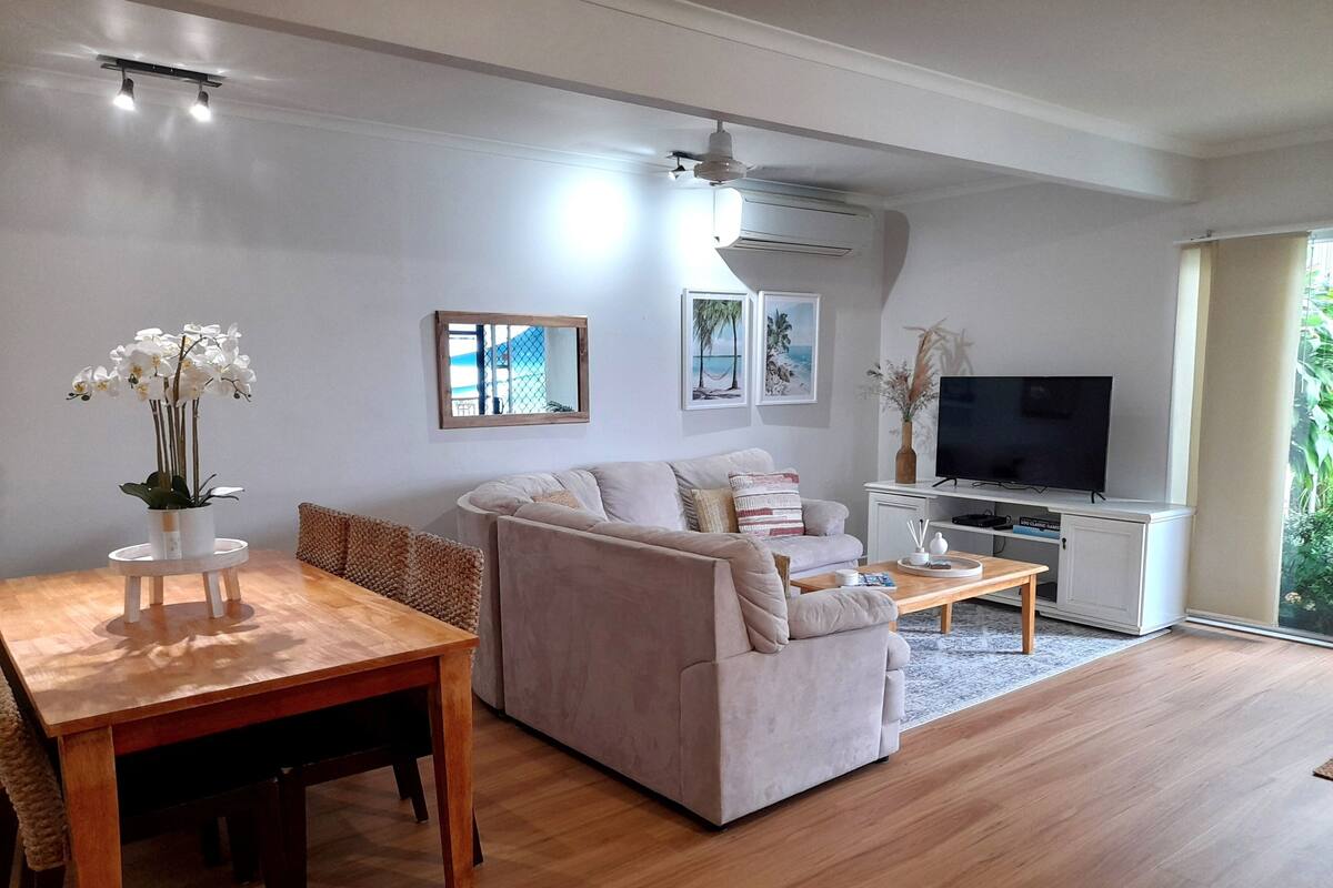 Een moderne woonkamer met een bank, een eettafel, een televisie en een groot raam.