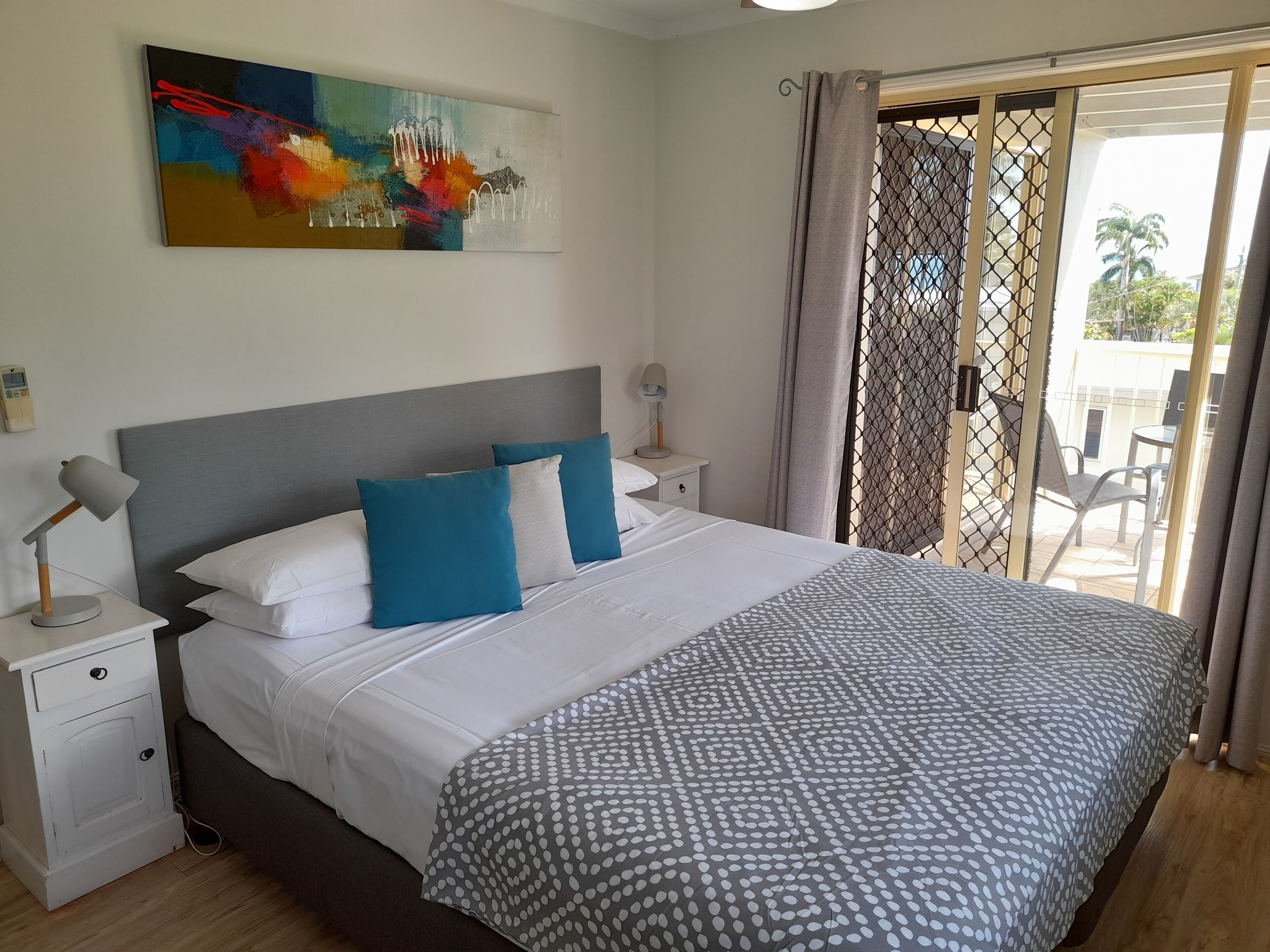 A neatly made bed with white and blue pillows, a grey patterned throw, and a modern headboard.