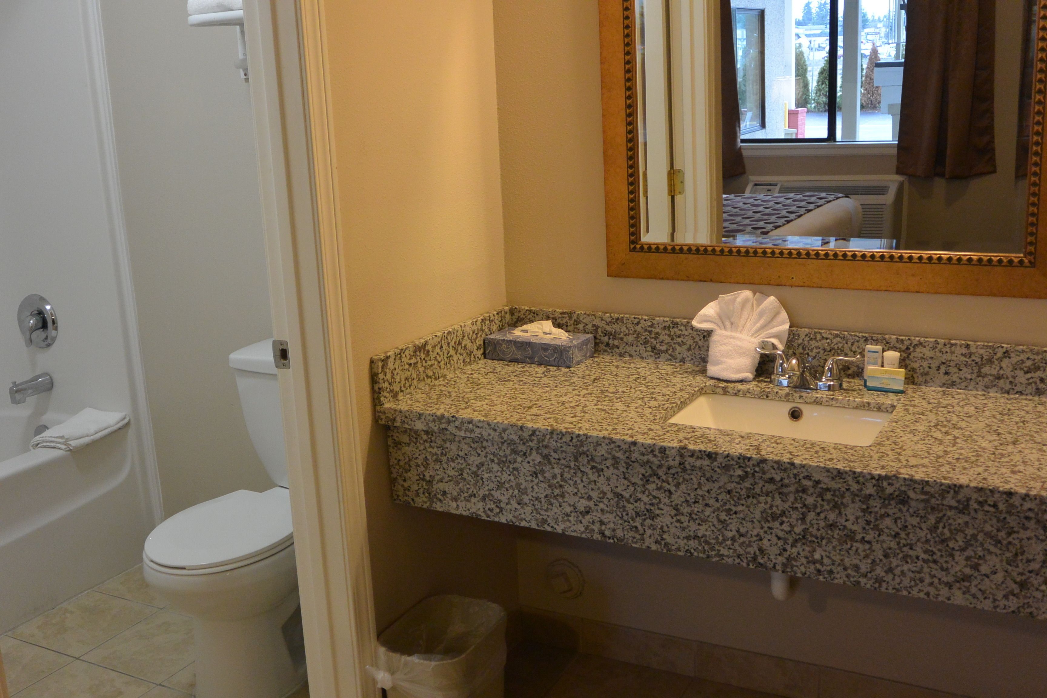 A bathroom with a granite countertop sink, a mirror, a towel, and a trash can.