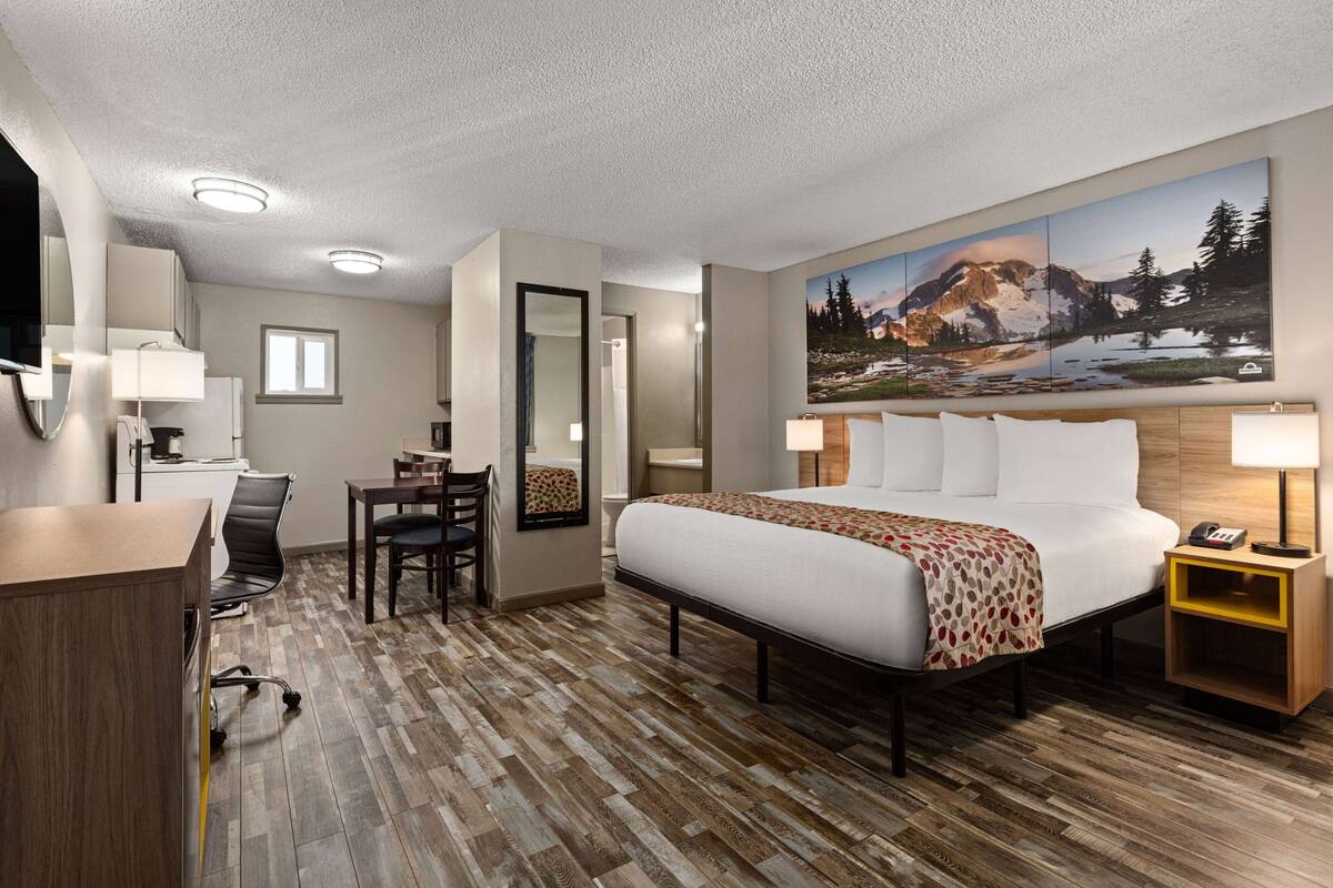 Habitación de hotel con cama, escritorio, silla y un cuadro de un paisaje montañoso.