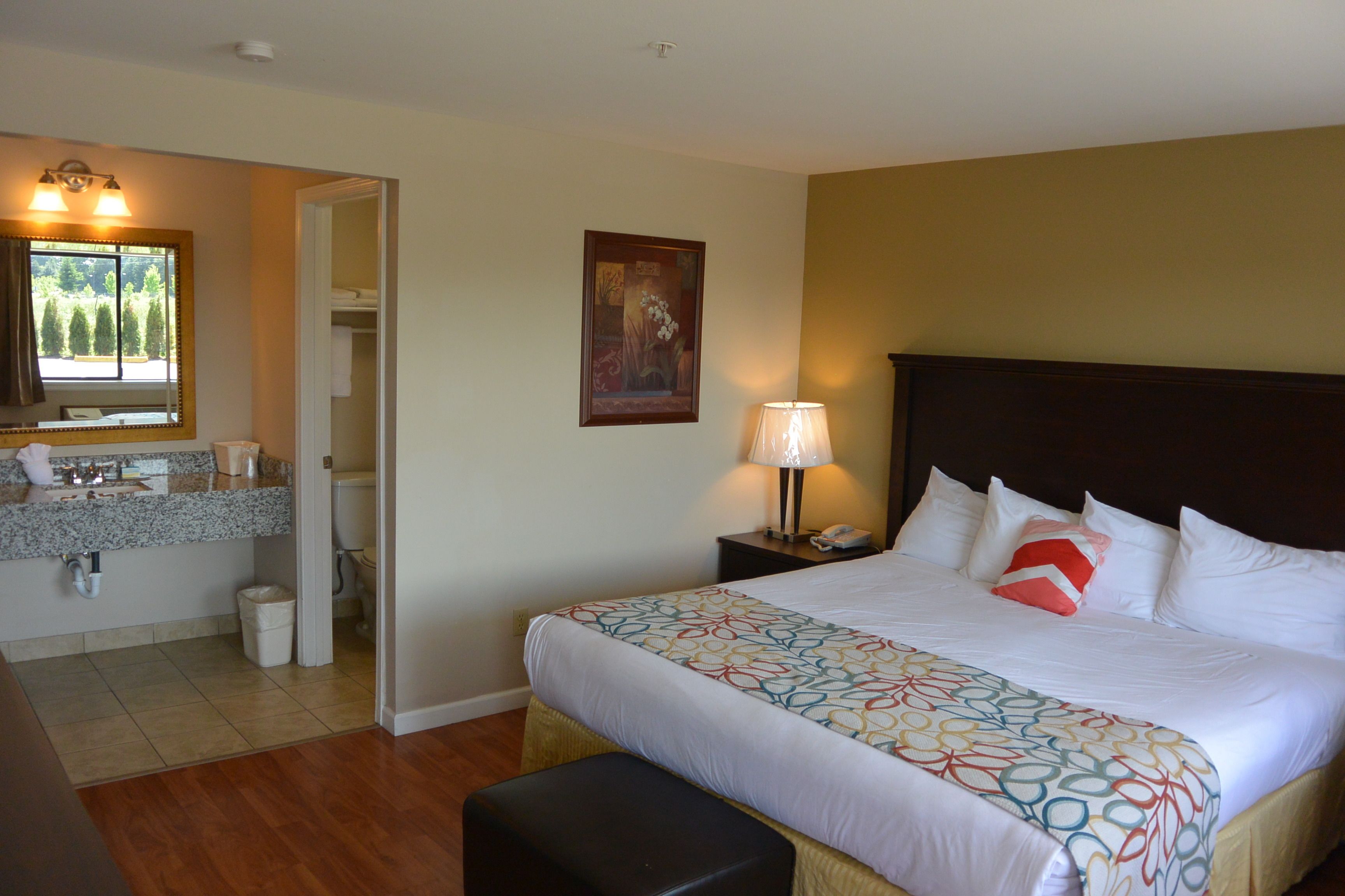 A hotel room with a bed, a nightstand, a lamp, a bathroom with a sink, and a mirror.