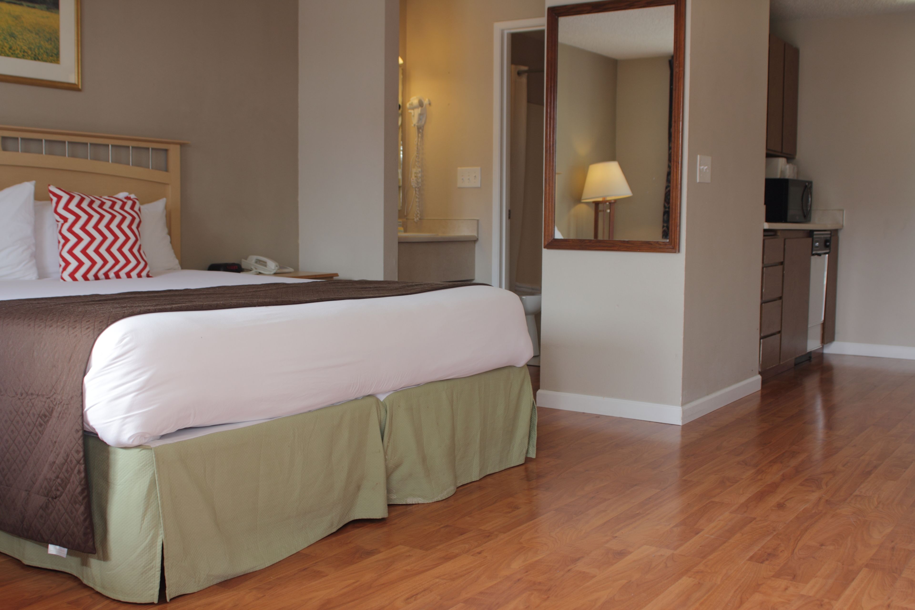 A hotel room with a large bed, a bedside table, a telephone, a mirror, and a kitchenette area.