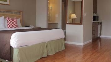 A hotel room with a large bed, a bedside table, a telephone, a mirror, and a kitchenette area.