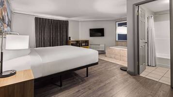 A hotel room with a bed, bedside table, lamp, TV, and a bathroom with a bathtub and shower.