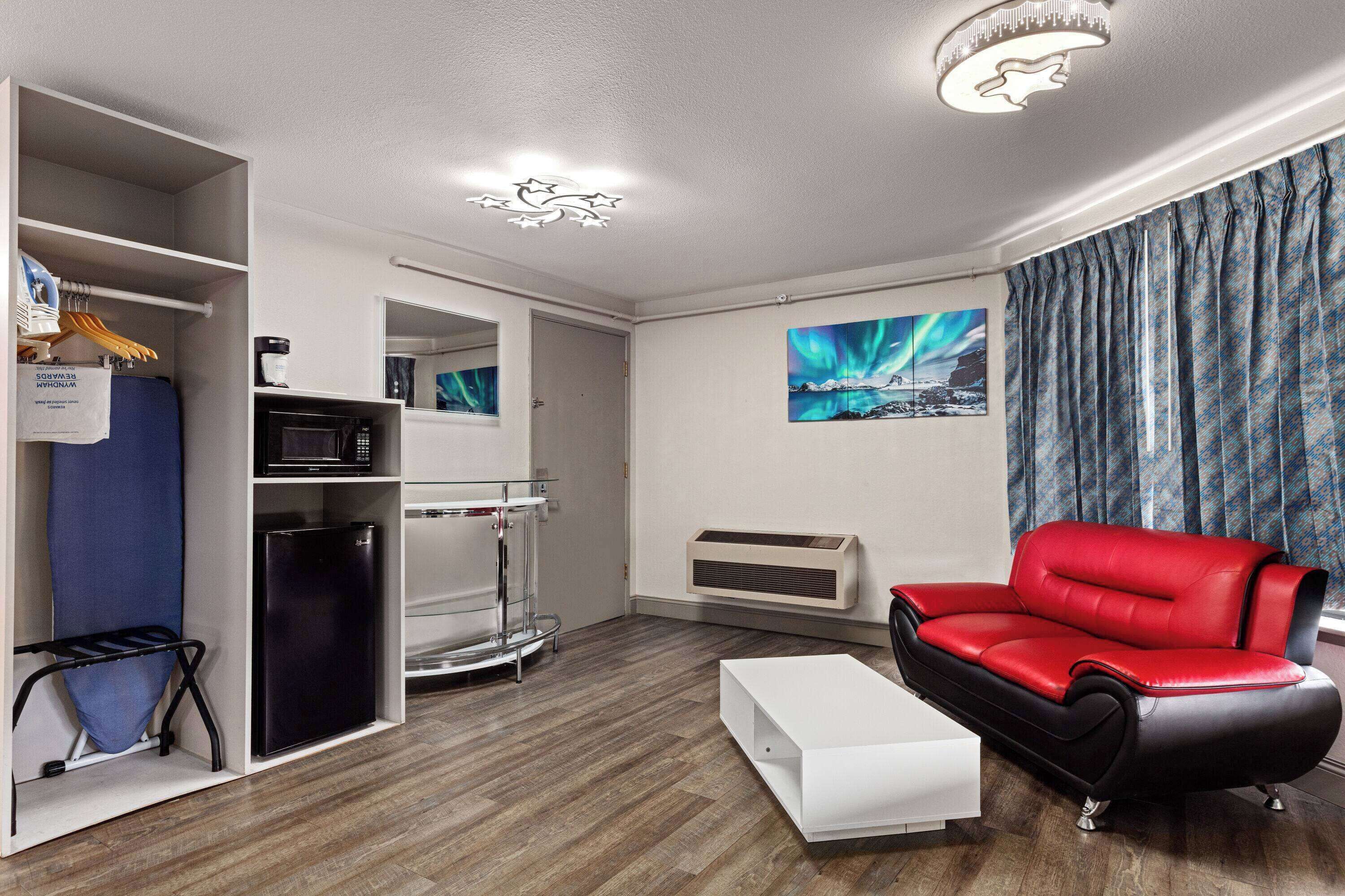 A modern living room with a red leather sofa, a white coffee table, a built-in air conditioner, a microwave, and a small refrigerator.