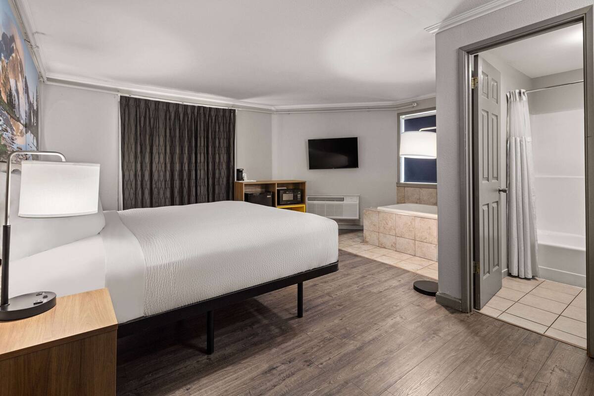 Una habitación de hotel con cama, escritorio, televisión, baño y ducha.