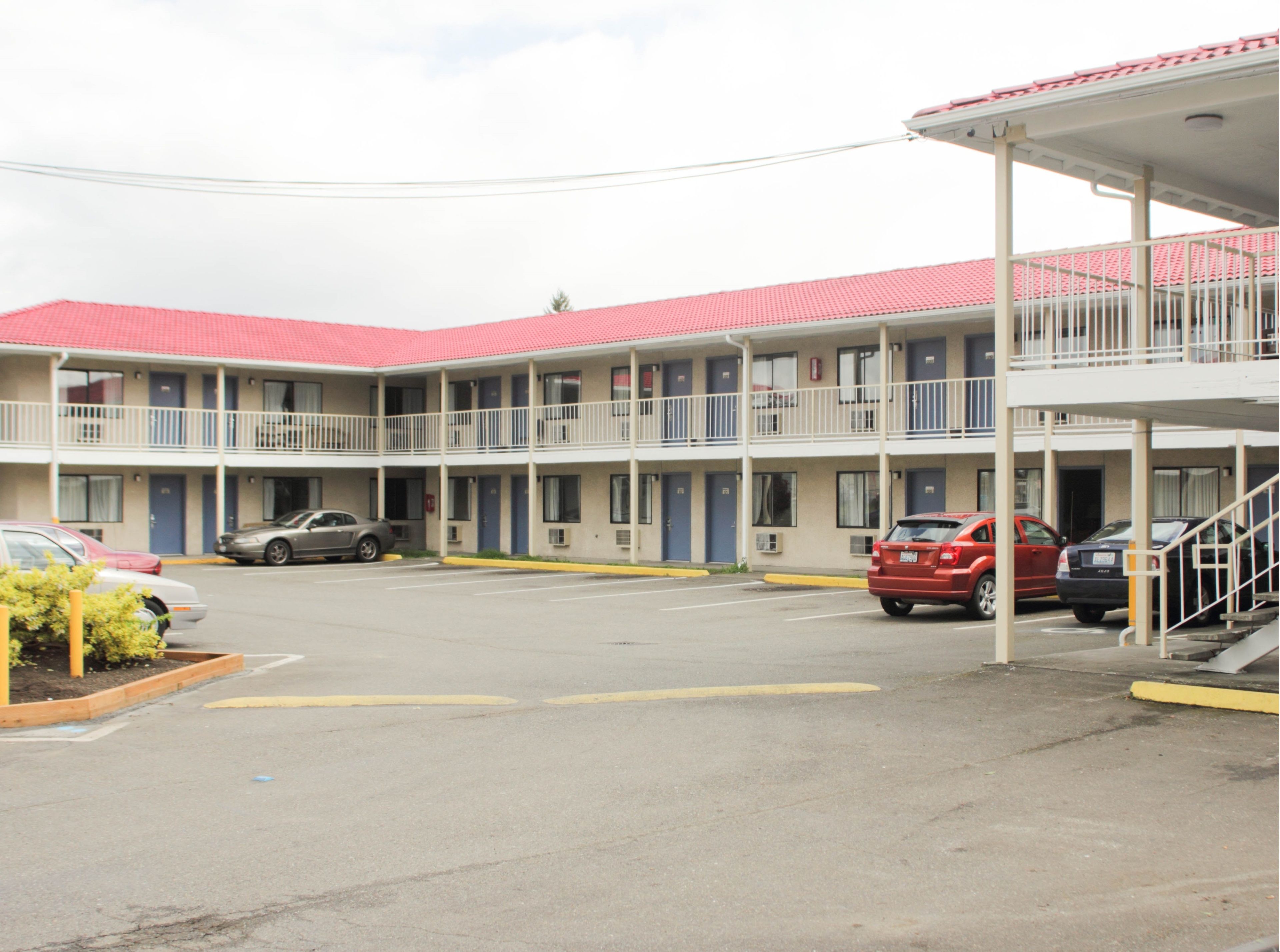 A motel with a red roof and multiple balconies. There are several cars parked in front.