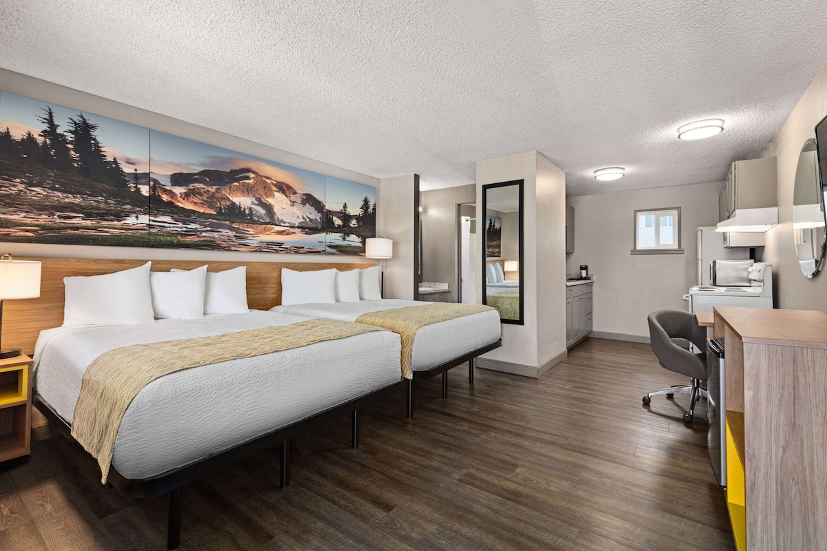 Habitación de hotel con una cama grande, un escritorio, una silla, un espejo y un cuadro de un paisaje montañoso.