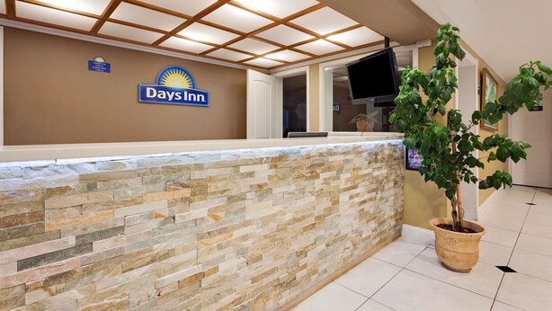 Een receptiegedeelte met een Days Inn bord, een stenen muur, een potplant en een flatscreen televisie.