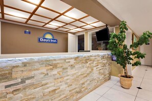 Una zona de recepción con un letrero de Days Inn, una pared de piedra, una planta en maceta y un televisor de pantalla plana.