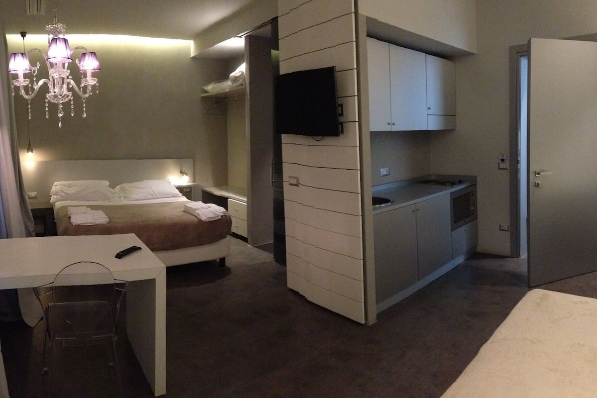 Une chambre d’hôtel de taille réduite, comprenant un lit, une table de chevet et une petite kitchenette.