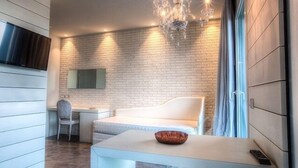 A modern hotel room with a white brick wall, a white sofa, a desk, and a chandelier.