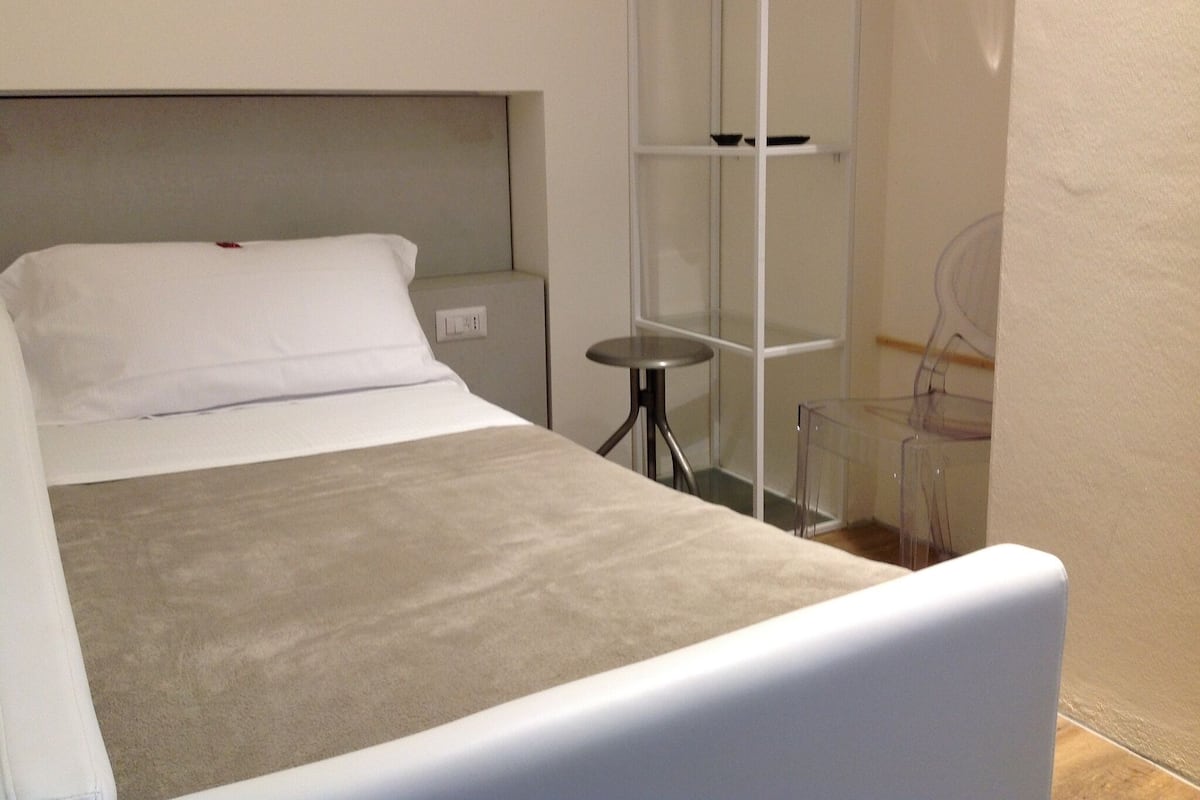 Une petite chambre à coucher, bien rangée, avec un lit, une table de chevet et une étagère.