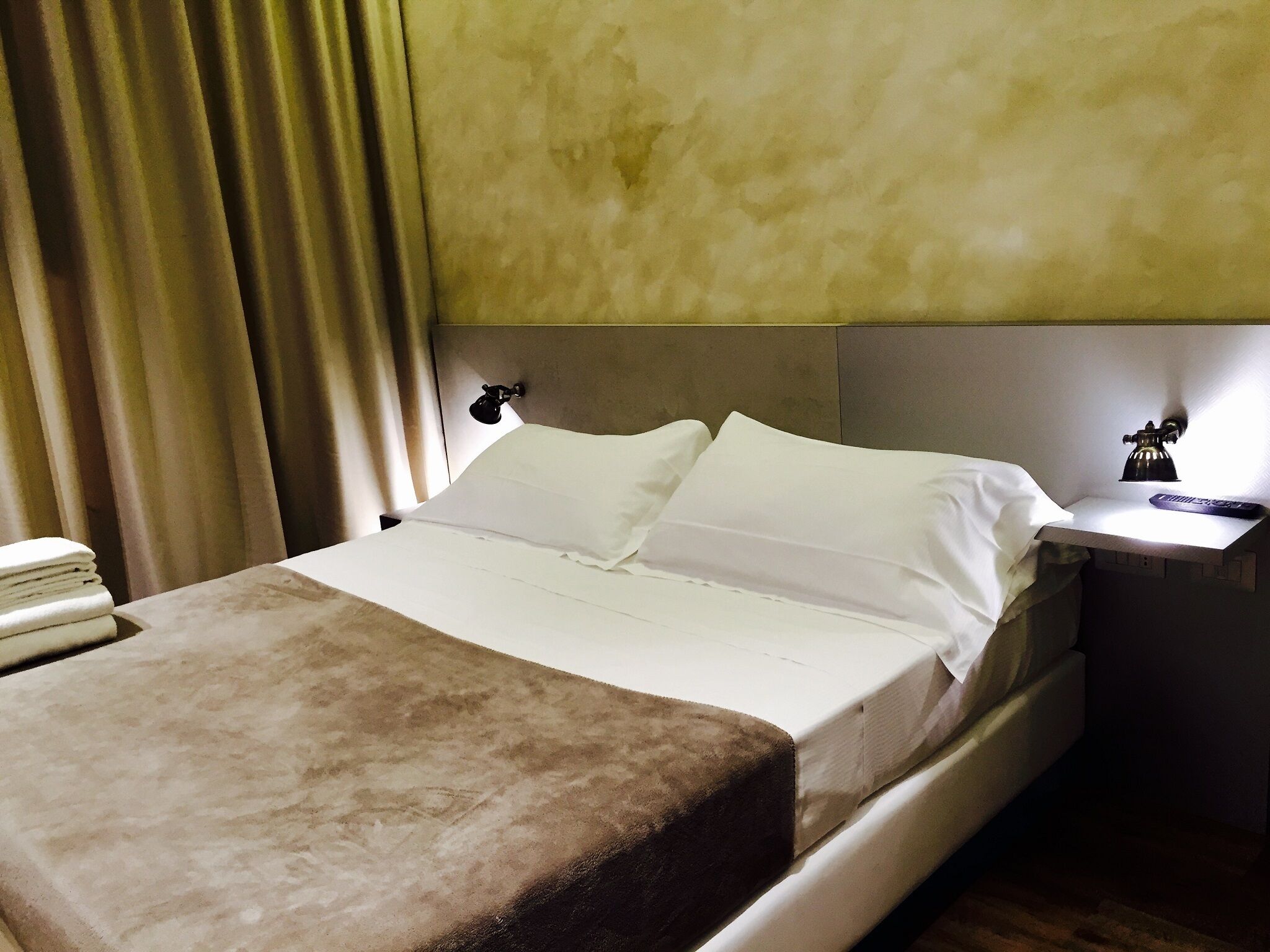 Ein Hotelzimmer mit Bett, Nachttisch und Lampe, sowie einem Vorhang.