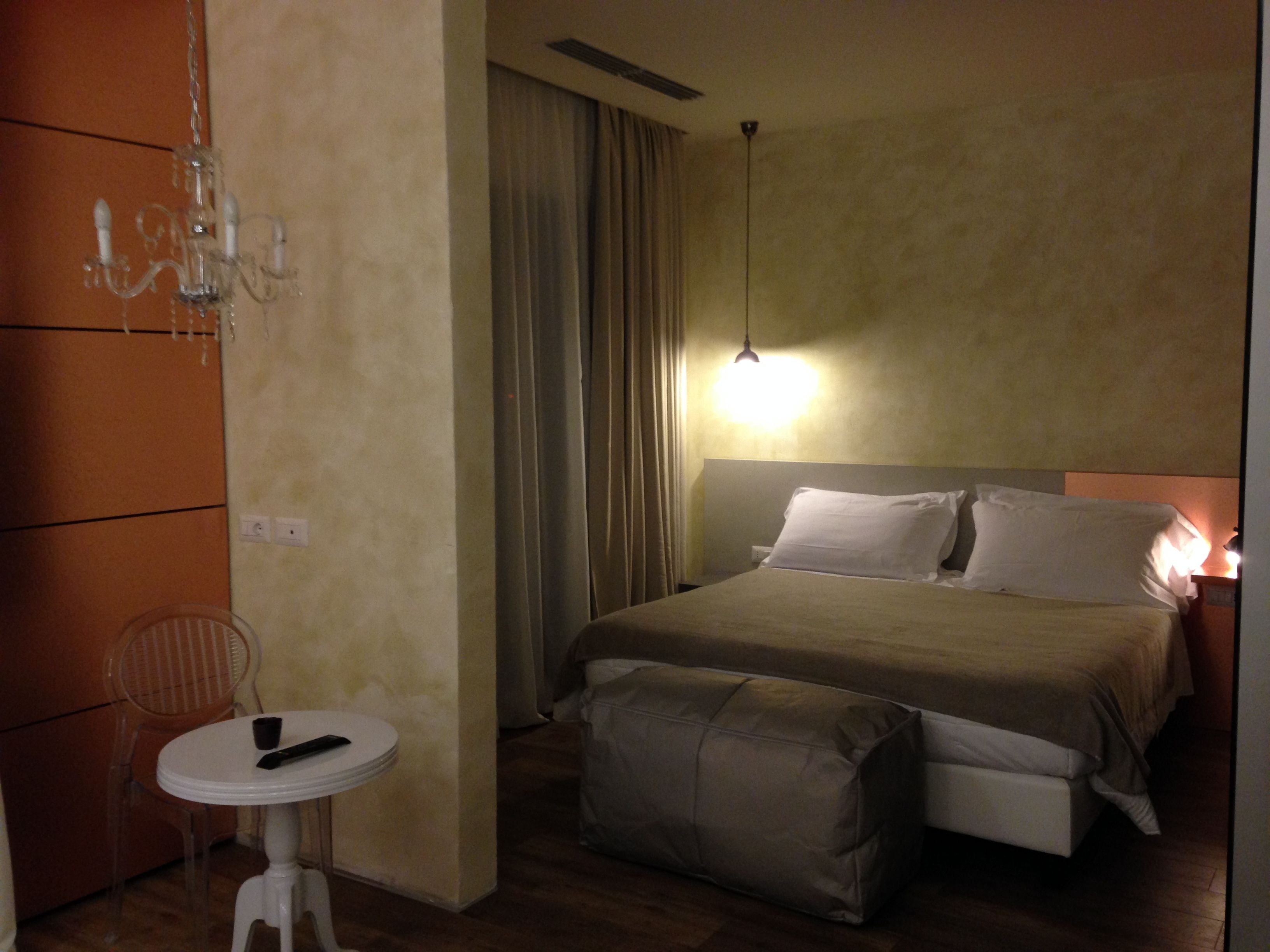 A hotel room with a bed, bedside table, chair, and a hanging light fixture.