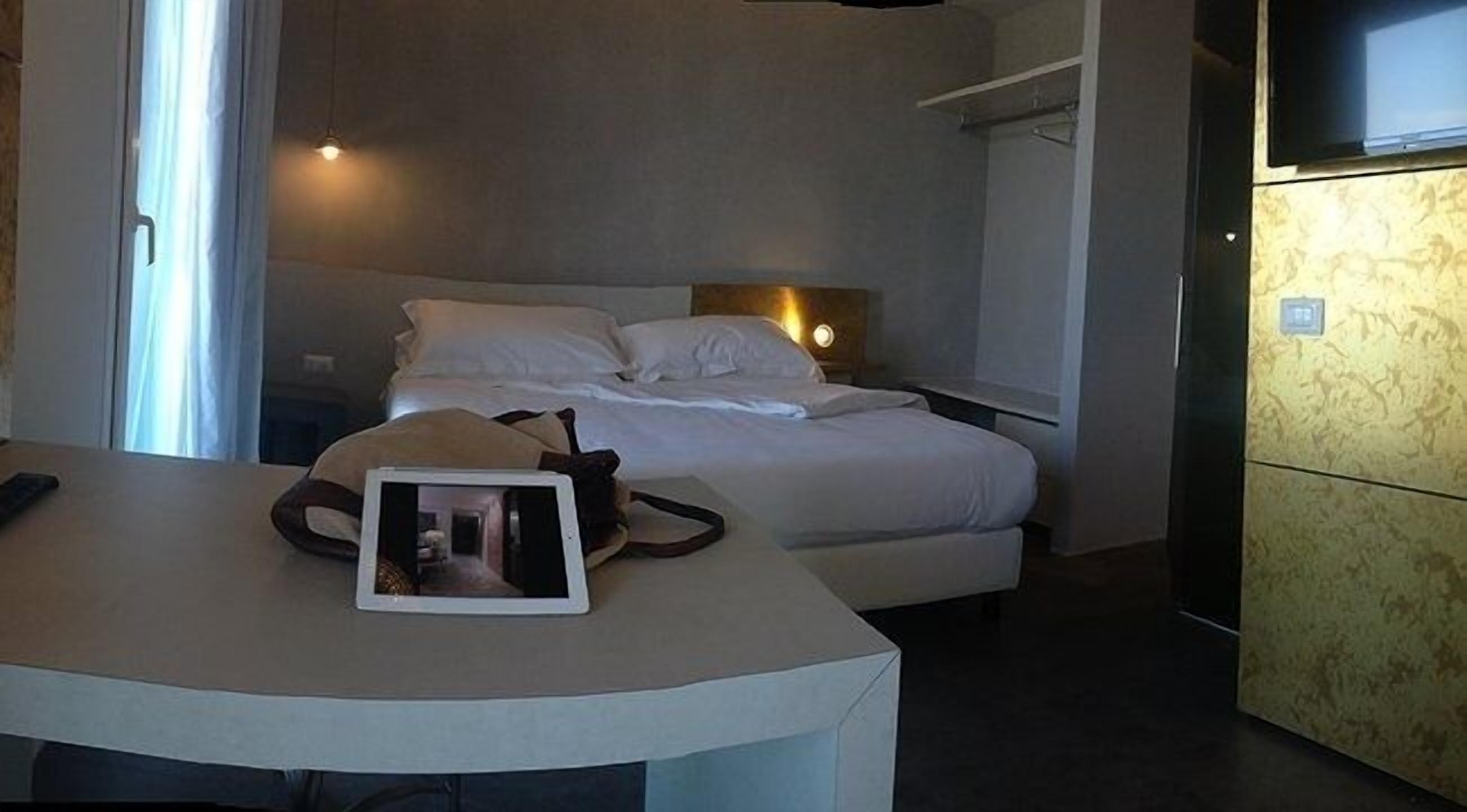 Una habitación de hotel con una cama, mesita de noche y televisión instalada en la pared.