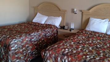 Habitación de hotel con dos camas, cada una con colcha estampada, cabecero de madera, mesita de noche y lámpara de pared.