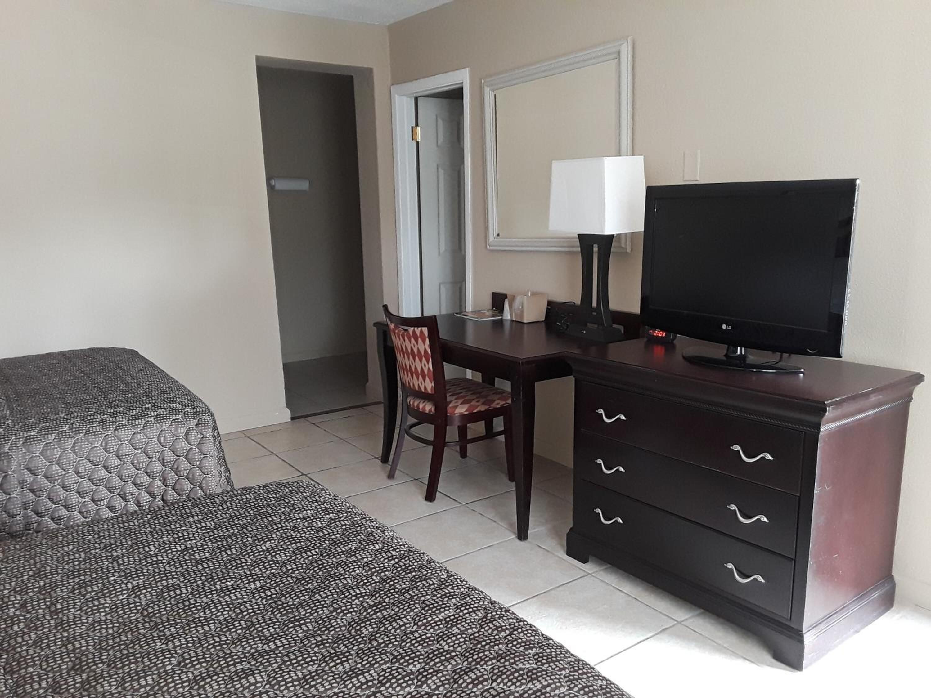 Habitación de hotel con cama, escritorio con televisor, silla, cómoda y ventana.