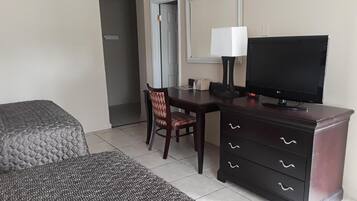 Habitación de hotel con cama, escritorio con televisor, silla, cómoda y ventana.