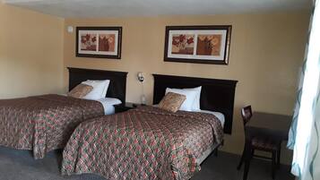 A hotel room with two beds, each with patterned bedspreads, a desk, and two framed pictures on the wall.