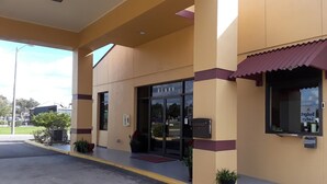 A building with a beige facade, a black entrance door, and a small awning. - Budget Lodge of Mount Dora (Mount Dora)